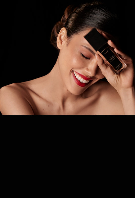 A radiant woman smiles while holding the TresMonet Rejuvenating R+ Complex bottle to her forehead. The product features a sleek black and gold design, highlighted as a NEW YOU Beauty Awards Winner 2022. This award-winning serum contains 0.1% Retinol, Vitamin C, and stem cell technology to promote youthful, radiant skin by evening tone, reducing redness, and minimizing fine lines and wrinkles.